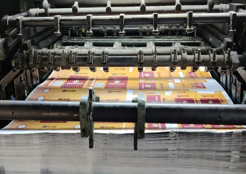 A large industrial printing machine in operation, showing sheets of colorful papers that are being printed.