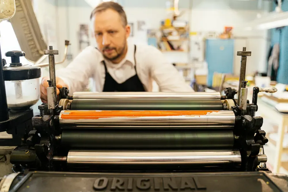 Close-up of a printing press with a man focused on the machinery.